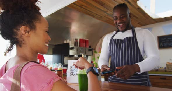 African american woman making payment from her smartwatch at the food truck alt