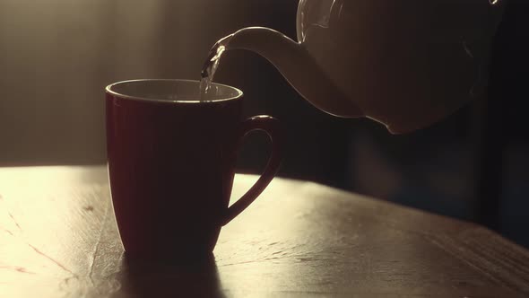 A Hand Pours Hot Tea From a Teapot Into a Mug