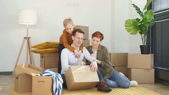 Young Caucasian Family Moving to New Place Sitting Holding Marker Pen Writing Carboard Boxes