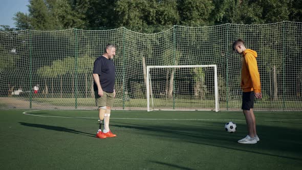 Wide Shot Positive Mature Amputee and Teenage Boy Playing Soccer in Slow Motion on Sunny Summer Day alt