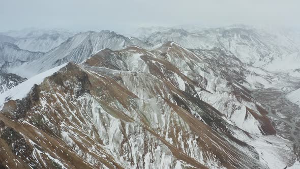 Drone Over Snowy Mountain Peaks With Braided Riverbed Below alt