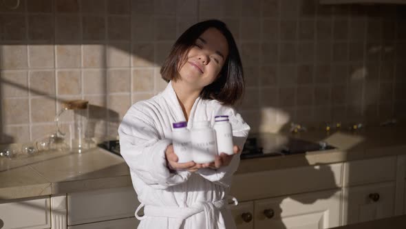 Smiling Adult Little Woman Posing with Vitamin Bottles in Kitchen at Home on Sunny Morning alt