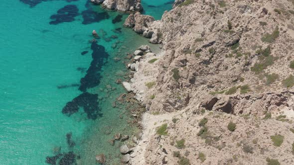 Overhead Top Down Aerial Flight Over Greek Island Mykonos Turquoise Blue Ocean with Rocky Cliff alt