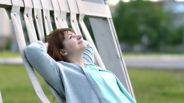 Happy Woman Relaxes Outdoors on a Bench in the Evening in the Park Happy News Sunny Weather