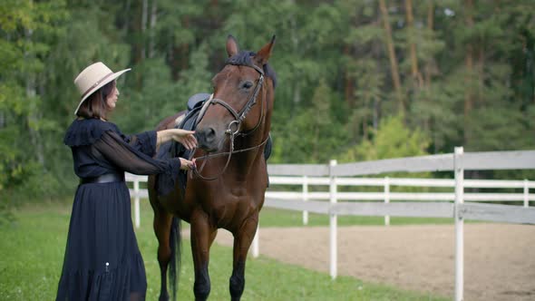 Beautiful Woman in Hat with Brown Horse on Farm Ranch. Attractive Woman Posing with Purebred alt