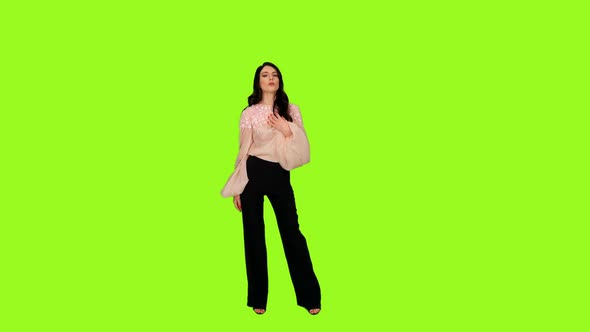 Young Stylish Brunette Female Dancing While Singing Song Against a Green Background