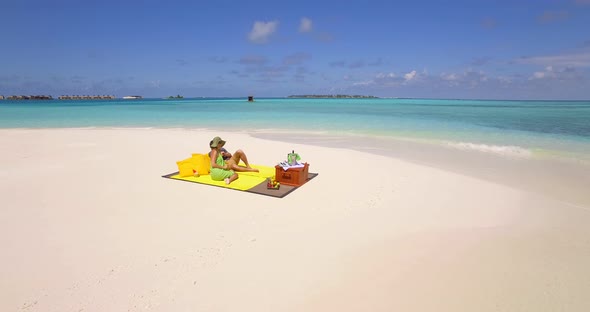 Aerial drone view of a man and woman couple having a picnic meal on a tropical island beach alt