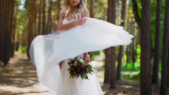 Pretty Bride Waves Skirt Holding Flowers Bouquet in Park alt