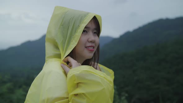 Young Asian woman feeling happy playing rain while wearing raincoat walking near forest. alt