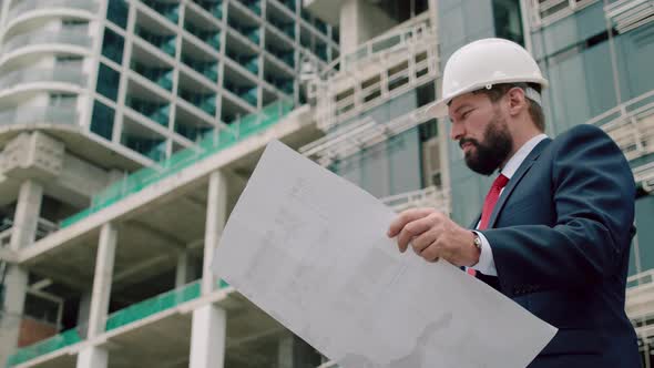 Engineer Male in a White Safety Helmet Developer at a Construction Site Checks on the Drawings at alt