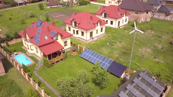 Aerial View of a Residential Private House with Solar Panels on Roof and Wind Generator Turbine alt