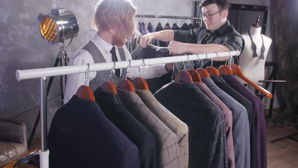 The Seller Helps a Young Elegant Man To Choose a Classic Suit in the Store