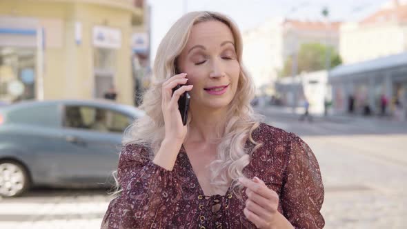 A Middleaged Caucasian Woman Talks on a Smartphone in an Urban Area alt