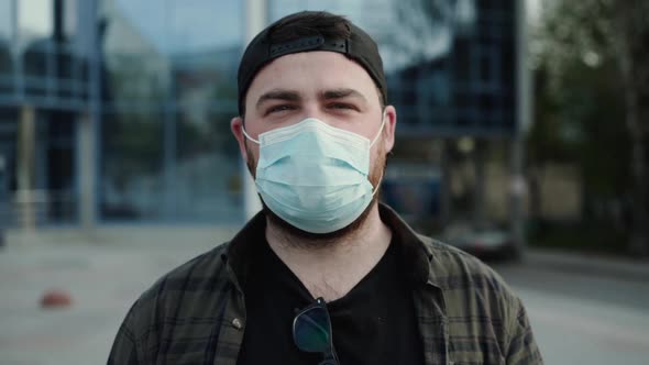 Young Man in Casual Clothes in Medical Mask Talking Into Camera with Gestures alt