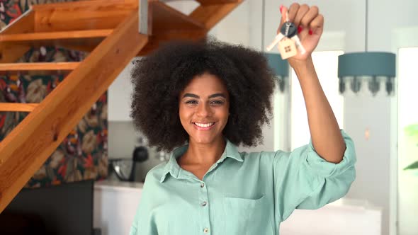 Happy Young Woman with Afro Hairstyle Holding Keys with Keychain in Form of Little House Indoors