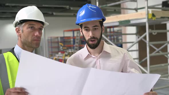 Male architect discussing with blueprint at construction site