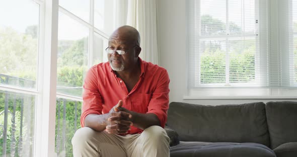 Happy senior diverse couple wearing shirts and drinking coffee in living room alt