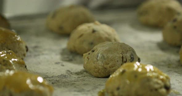 Baker Applying Egg Wash With A Pastry Brush To Raisin Cookies On A Tray Before Baking - slow motion alt