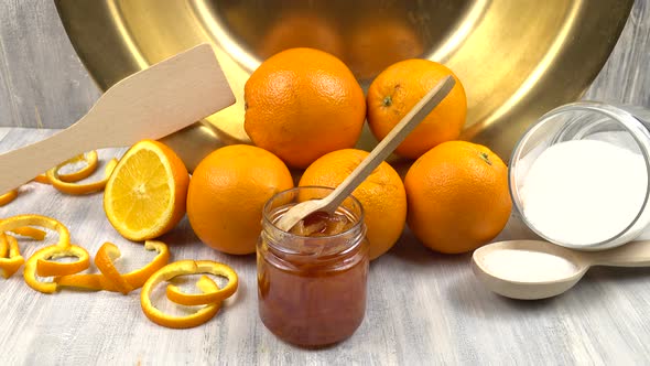 Oranges, sugar, a jar of jam and a copper bowl for making jam are on the kitchen table. alt