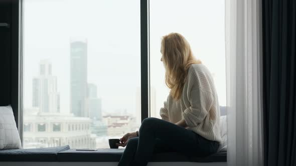 beautiful blonde woman drinking tea while sitting by the window