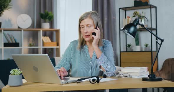 Senior Business Woman Talking on Mobile and Typing on Laptop alt
