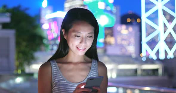 Woman Looking at Mobile Phone in City at Night  alt