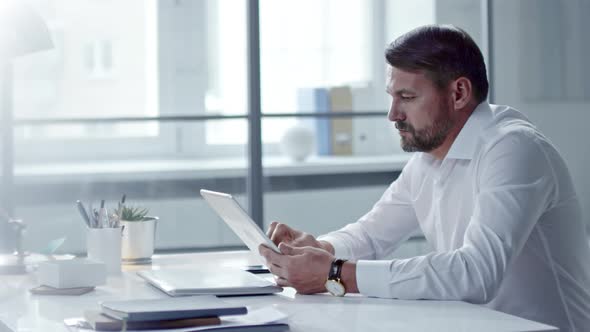 Mid-Aged Businessman Surfing the Net on Tablet alt