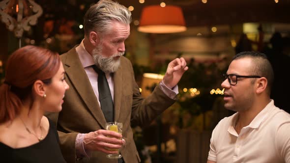 A gray-haired adult respectable man tells something to friends near the bar alt