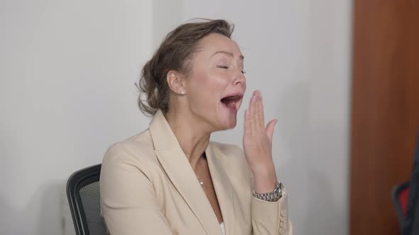 Tired Caucasian Beautiful Woman Yawning Sitting Indoors in Office alt
