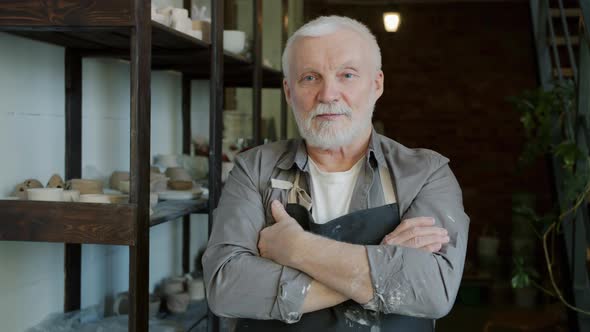 Portrait of Handsome Elderly Man Potter Standing in Workshop Wearing Apron and Looking at Camera alt