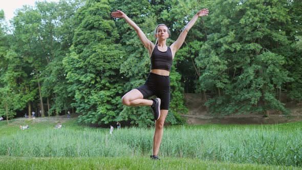 Slim Blonde Woman Does a Stretching Exercise Standing Yoga Pose in City Park alt