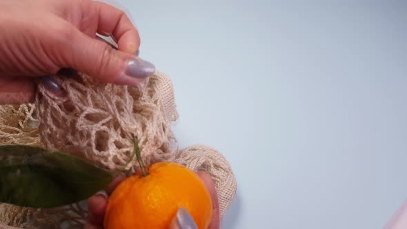 Hands take out tangerines from a white reusable food mesh bag