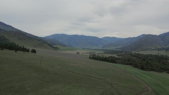Rural fields and mountains under blue sky with white clouds in Altai