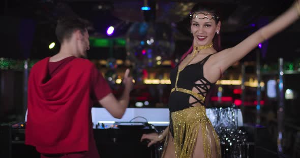 Back View of Young Caucasian DJ Playing Music in Night Club As Beautiful PJ Dancing Next To Him alt