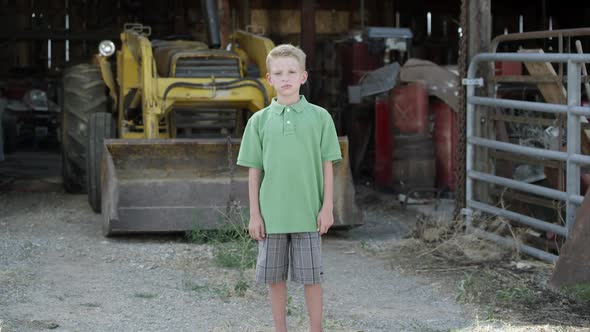 Slow motion push of boy with cleft lip standing in front of tractor. alt