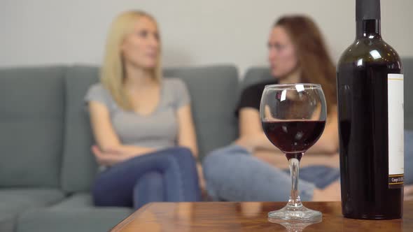 Two girls chat at home and drink red wine. alt