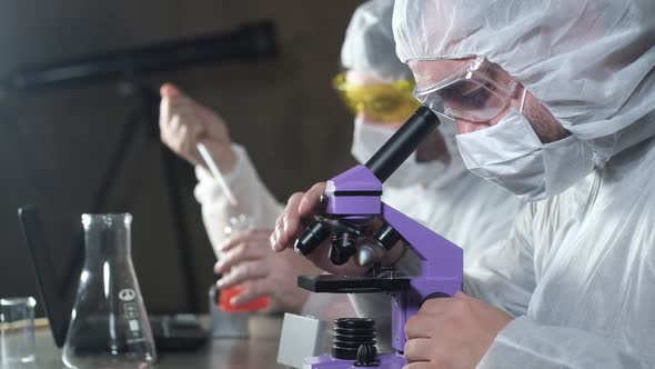 scientists in lab wearing protective masks use a microscope for research. alt