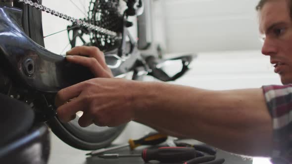 Focused caucasian man repairing bike using tools in garage alt