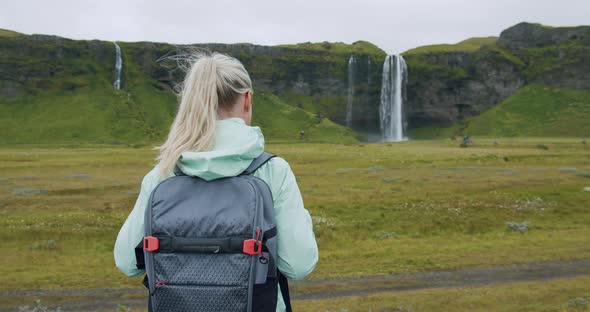 Woman with Backpack Looking at Seljalandsfoss Waterfall Iceland alt