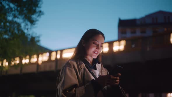 Young woman laughing while typing into her phone at night alt