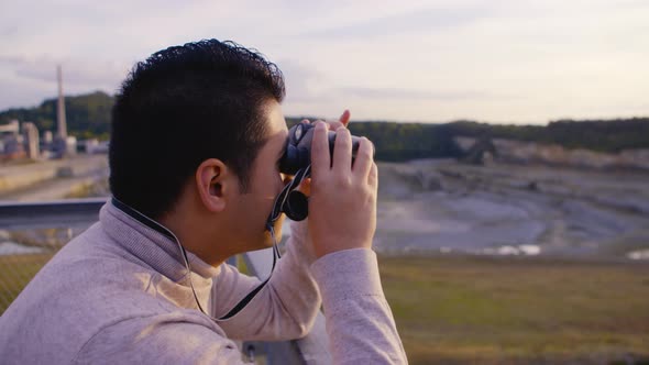 A young man looking over a beautiful scenery of a quarry with binoculars alt