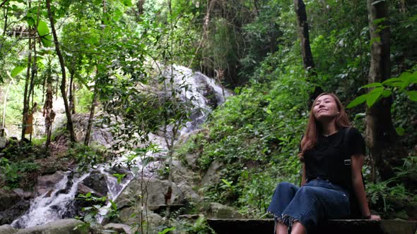 A young asian woman relaxing and sitting by the waterfall