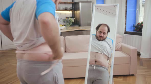 Fat Man with Measuring Tape Standing at Mirror alt