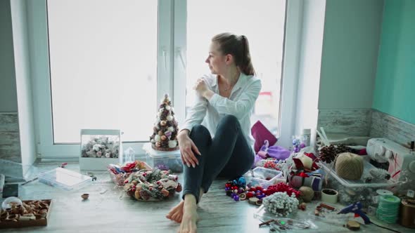 Girl is Sitting By Window Around Her Scattered for Christmas Decorations alt