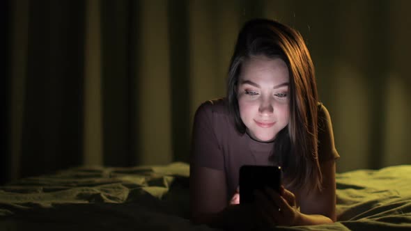 Young Woman Browsing Smartphone Watching Social Media Lying in Bed Front View