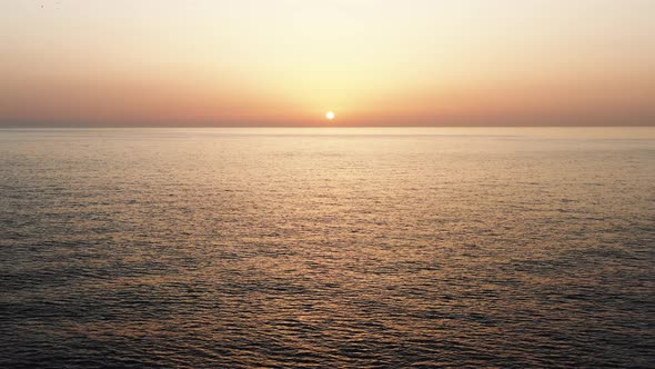 Drone Flying Backwards From Atmospheric Sunset Over Rippled Sea with Birds Flying Around alt