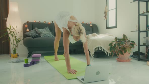 Woman Doing Stretching on the Floor at Home in Front of Her Laptop Online Yoga Class alt