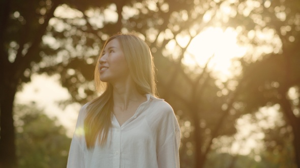 A beautiful young Asian female enjoying the breeze forest in the public park during sunset.