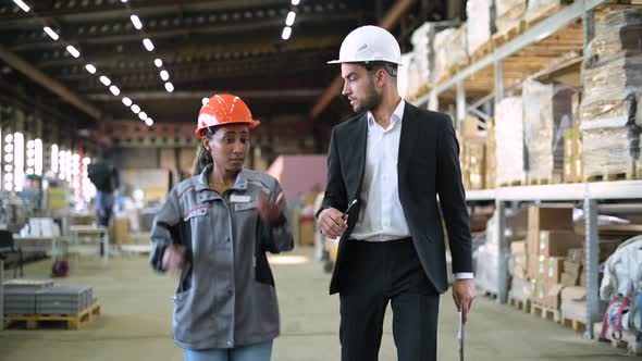 White man, boss and black woman, worker, walk through the production workshop alt