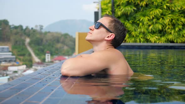 Handsome Man in Sunglasses Leans on Hotel Pool Edge alt